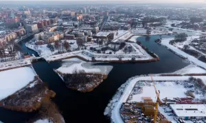 Zimowy krajobraz dolnego miasta Gdańsk z rzeką, ośnieżonymi budynkami i placem budowy z dźwigami.