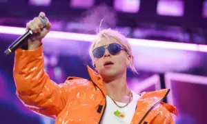 Artysta w pomarańczowej kurtce z mikrofonem, w okularach przeciwsłonecznych. Ciekawe, ile skolim bierze za koncert, że stać go na taki strój!