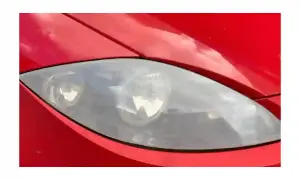 Gros plan sur un phare opaque de voiture rouge, reflétant le ciel.