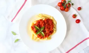 Penne pomodoro z bazylią na białym talerzu, obok gałązka pomidorków koktajlowych.