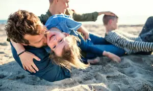 Rodzina na plaży, ojciec tuli córkę, która śmieje się do aparatu. W tle mama i syn. Idealne miejsce na jastrzębia góra atrakcje dla dzieci.