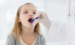 Niña con la boca abierta, examinada por un médico. Podría ser una consulta previa a una **operación amígdalas niños**.