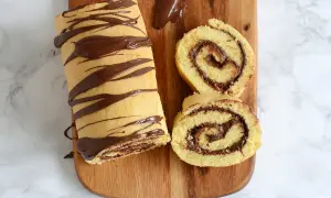 Un roulé au Nutella, entier et tranché, décoré de chocolat fondu sur une planche en bois. Un délice gourmand !