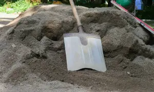 Łopata wbita w kopiec suchego betonu, obok poziomica.