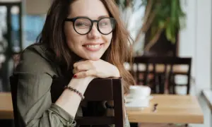 Uśmiechnięta młoda kobieta w okularach opiera się o krzesło.
