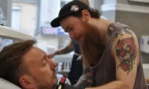 Artysta z tatuażem tygrysa na ramieniu wykonuje nowy wzór. Czy prokurator może mieć tatuaże? Ten artysta z pewnością je ma!