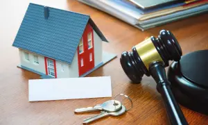 Modellino di casa, chiavi, martelletto da giudice e documenti su un tavolo di legno, evocano aste immobiliari tra privati.