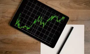 Tablet z wykresem zielonej linii na czarnym tle, obok ołówek i kartka papieru. Analiza npv.