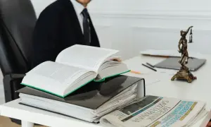 Prawnik w garniturze studiuje prawo, obok otwarty kodeks, akta i Dziennik Gazeta Prawna. Czas na vacatio legis.
