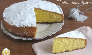 Una soffice torta paradiso, cosparsa di zucchero a velo, attende di essere gustata. Una fetta è già pronta su un tovagliolo rosa.