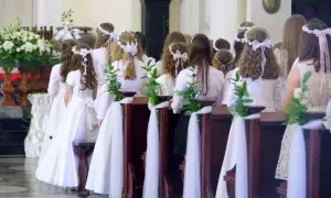Dzieci w białych strojach, ozdobione wiankami, czekają na komunię. Zazwyczaj do komunii idzie się w wieku około 8-9 lat.