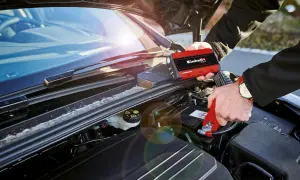 Person kopplar startkablar till bilbatteri. En röd Einhell-enhet används för att ge ström, perfekt för dieselbilar som behöver en extra knuff.