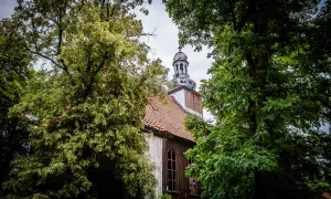 Stary kościół w Miejskiej Górce, otoczony bujną zielenią drzew, z charakterystyczną wieżą i drewnianą elewacją.