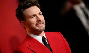 Chris Evans w czerwonym garniturze, jak z najlepszych filmów. Uśmiechnięty, z zarostem, prezentuje się elegancko.