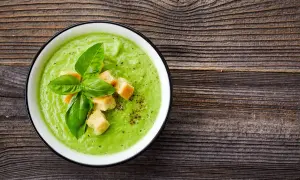 Un cremoso passato di verdure verde brillante, guarnito con crostini dorati e basilico fresco, su un tavolo di legno rustico.