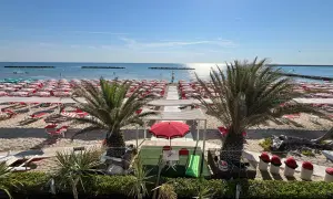 Spiaggia di Porto San Giorgio mare con file ordinate di ombrelloni rossi e bianchi, lettini, palme e il mare azzurro sotto un cielo limpido.