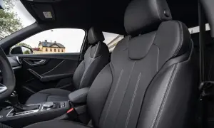 Interni Audi Q2: sedili in pelle nera con cuciture a contrasto, cambio automatico e un edificio storico sullo sfondo.