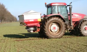 Czerwony traktor McCormick z rozsiewaczem nawozów, przygotowujący pole do wiosennych prac. Optymalne saletra wapniowa dolistnie dawkowanie zapewni zdrowy wzrost roślin.