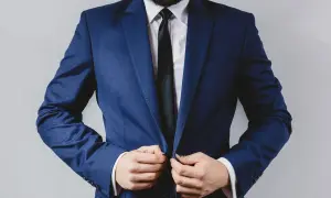 Mężczyzna w granatowym garniturze, białej koszuli i czarnym krawacie zapina marynarkę.