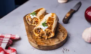 Dwa soczyste wrapy z kurczakiem, polane sosem i posypane natką pietruszki. Idealna shoarma z kurczaka na drewnianej desce.