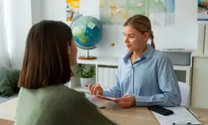 Doradca turystyczny pokazuje paszport klientce przy biurku z globusem i mapami.