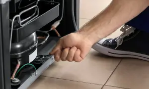Ręka z kluczem przy kompresorze lodówki. Pozwala to zrozumieć, jak działa lodówka i jej podstawowe elementy.