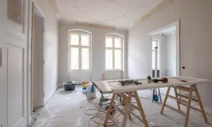 Mieszkanie na sprzedaż do remontu. Wnętrze w trakcie prac, widoczne materiały budowlane, drzwi na kozłach, okna i drzwi z żółtą taśmą.