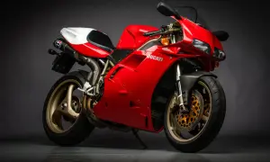 Czerwony motocykl Ducati z białym siedzeniem i złotymi felgami na ciemnym tle.