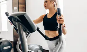 Junge Frau trainiert auf Crosstrainer, um ihren Kalorienverbrauch zu steigern.