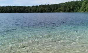 Jasne, krystalicznie czyste jezioro zaprasza do kąpieli. Piasek na dnie widoczny jest przez przejrzystą wodę.