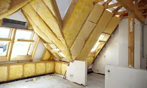 Budowa poddasza użytkowego w trakcie. Widoczne drewniane konstrukcje dachu, izolacja z wełny mineralnej i okna dachowe.