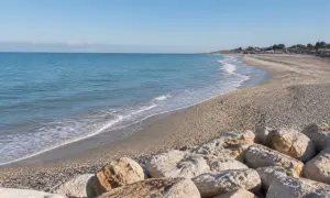 Spiaggia di Porto Sant'Elpidio Mare con rocce in primo piano e mare calmo sotto un cielo azzurro.