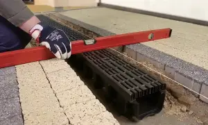 Rękawica z poziomicą sprawdza montaż odpływu w garażu.