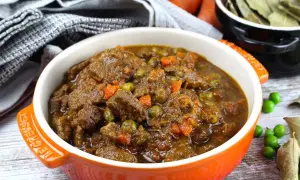 Ternera a la jardinera en un cuenco naranja, con trozos de carne tierna, guisantes y zanahoria en una rica salsa.
