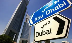 Znaki drogowe wskazują kierunek do Abu Zabi i Dubaju, na tle nowoczesnych wieżowców.