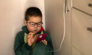Chłopiec w okularach i piżamie z dinozaurem skupiony na telefonie. Czas na ekranie to wyzwanie, ale warto pamiętać o ograniczeniu czasu na telefonie.