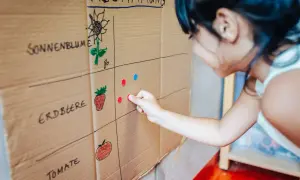 Kind übt Demokratie im Kindergarten: Es wählt per Klebepunkt seine Lieblingsfrucht auf einer selbstgemalten Abstimmungstafel.