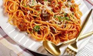 Spaghetti z bakłażanem i pomidorami, polane bogatym sosem sycylijskim, posypane parmezanem i natką pietruszki. Złote sztućce czekają.