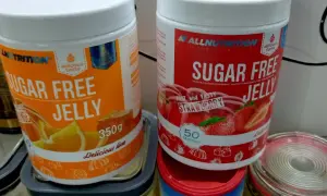Dwie puszki galaretki bez cukru: pomarańczowa i truskawkowa. Zastanawiasz się, ile kalorii ma galaretka truskawkowa? Te produkty są niskokaloryczne.