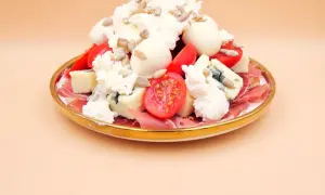 Sałatka z szynką parmeńską, serami, pomidorkami i słonecznikiem na złotym talerzu.
