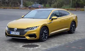 Złoty Volkswagen Arteon R z czarnym dachem i felgami, zaparkowany na bruku.