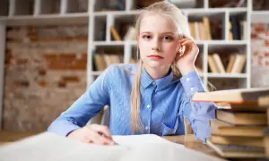 Młoda kobieta z blond włosami siedzi przy biurku, przed nią otwarte księgi. Przygotowuje wniosek o zwolnienie z kosztów sądowych.