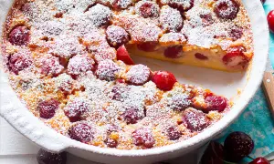 Clafoutis di ciliegie appena sfornato, cosparso di zucchero a velo, con una fetta mancante che rivela la morbida consistenza.