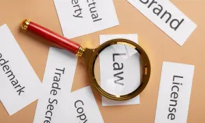 Lupa powiększa słowo "Law" wśród kart z napisami: "Brand", "License", "Copyright", "Trade Secret", "Trademark", "Intellectual Property". To symboliczne przedstawienie analizy prawnej wartości niematerialnych i prawnych.