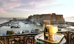En balkong med champagne och glas, med en vy över hamnen och Castel Nuovo i Neapel.