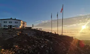 Sonnenaufgang über einer Wolkendecke, mit Hütte und Fahnen. Ein perfekter Moment auf der Sarntaler Hufeisentour.