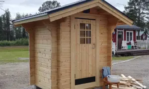 Nybyggt utedass i trä, redo att användas. Enkla verktyg och material ligger redo för att bygga utedass.