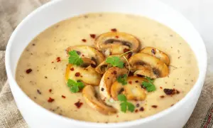 Aksamitny zupa krem z pieczarek, udekorowana plasterkami pieczarek, natką pietruszki i płatkami chili.