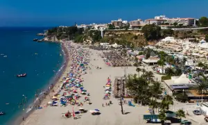 Vista aérea de la bulliciosa playa de Burriana, considerada la mejor playa de Nerja, con gente disfrutando del sol y el mar azul.