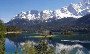 Idyllische Bergkulisse mit schneebedeckten Gipfeln, einem türkisfarbenen See und kleinen Inseln. Ein Boot gleitet über das Wasser, ideal für den Kramerplateauweg Rundweg.